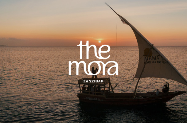 Small exotic sailing ship in front of sunset and logo of the mora zanzibar